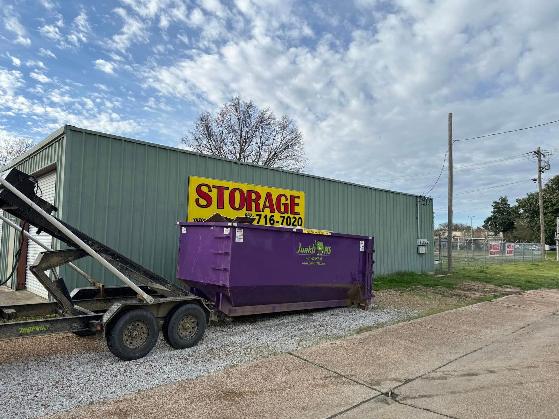 Purple dumpster on a trailer outside a storage building with a yellow 