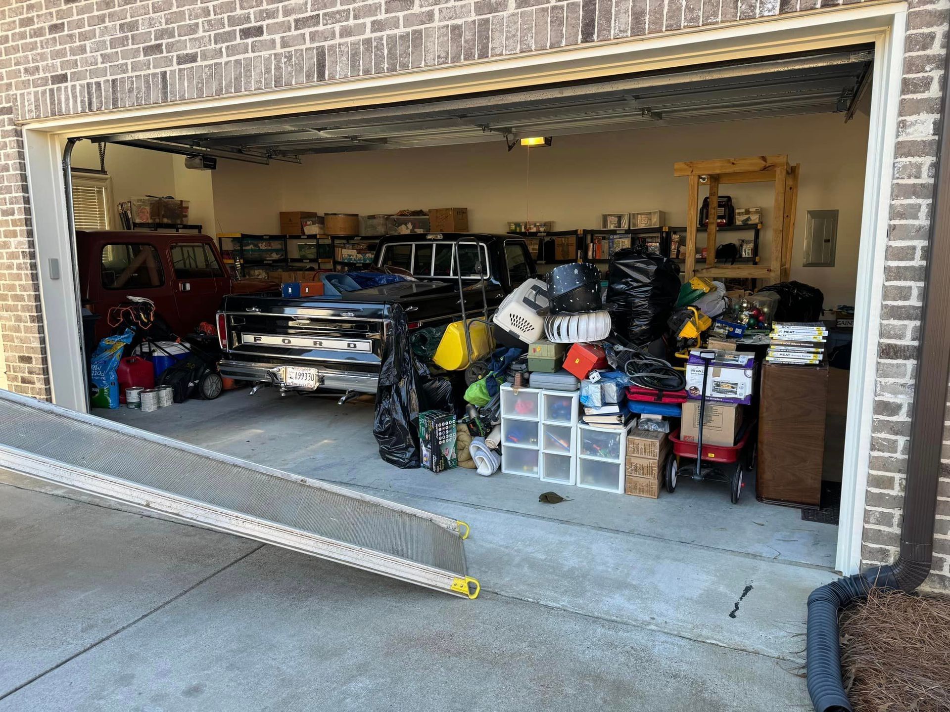 Cluttered garage with cars, boxes, and various items. A ramp leads into the space.