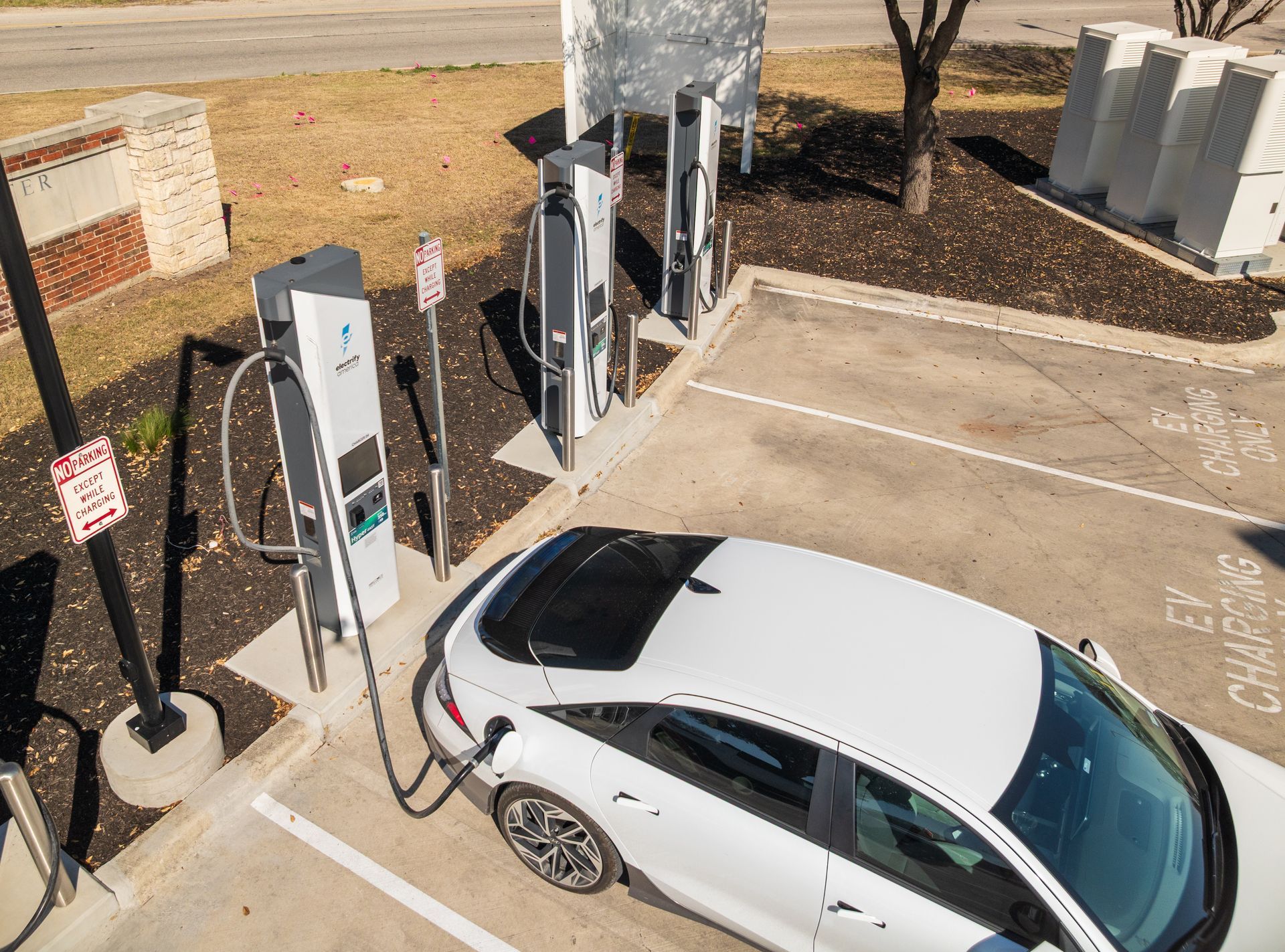 Une voiture électrique blanche branchée à une station de recharge publique avec plusieurs bornes de charge visibles dans un p