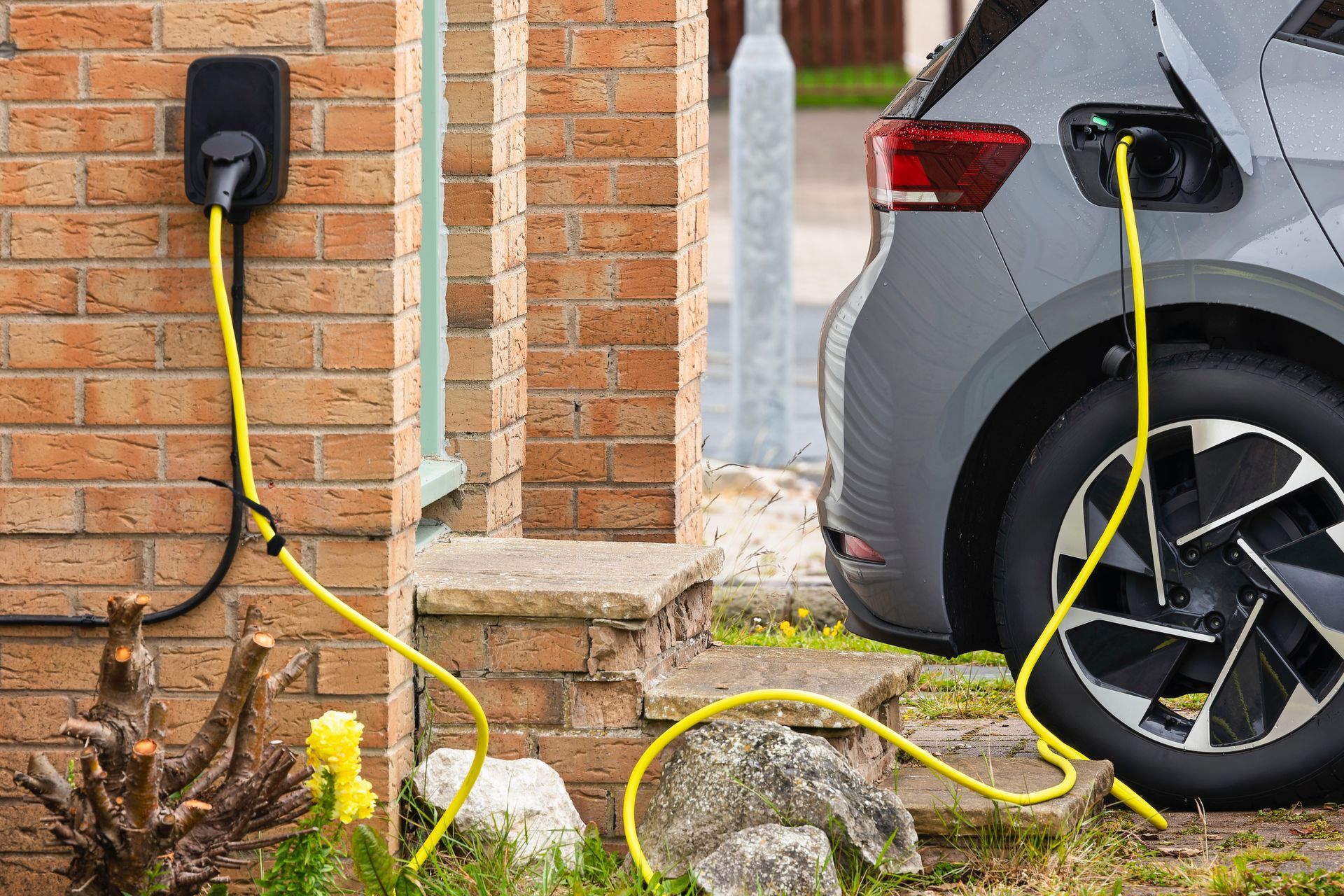 Recharge d’une voiture électrique devant une maison en briques, avec un câble jaune branché sur le véhicule.