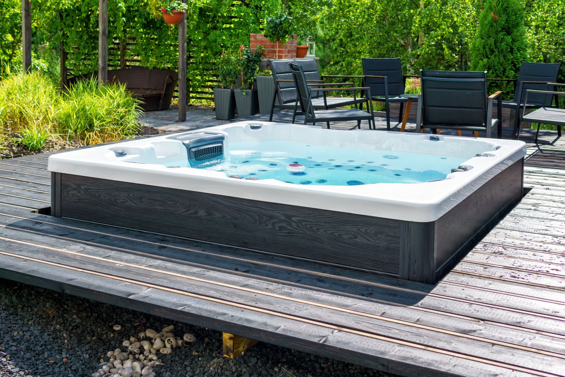 Petit bain à remous extérieur avec une eau bleue bouillonnante, installé sur une terrasse en bois entourée de chaises longues et de verdure