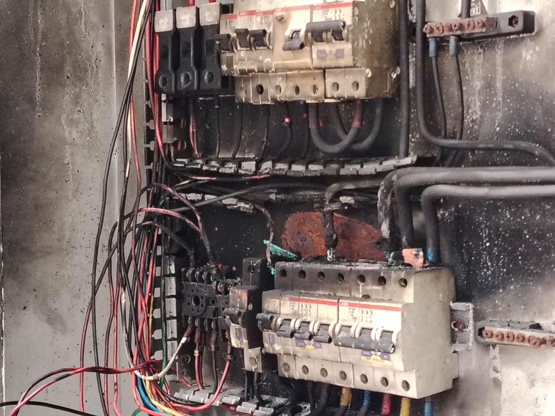 Tableau électrique brûlé avec des fils emmêlés et des disjoncteurs dans un boîtier endommagé