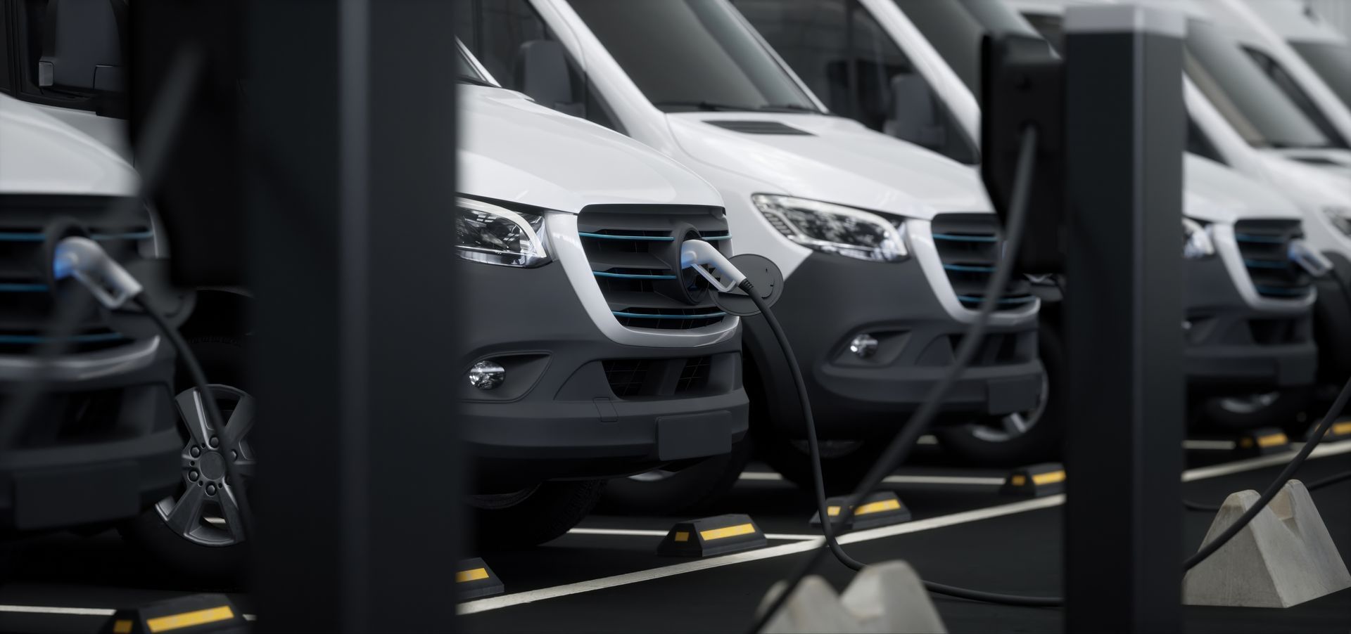 Rangée de fourgonnettes blanches en train de recharger sur une borne de parking, vues à travers des poteaux sombres au premier plan