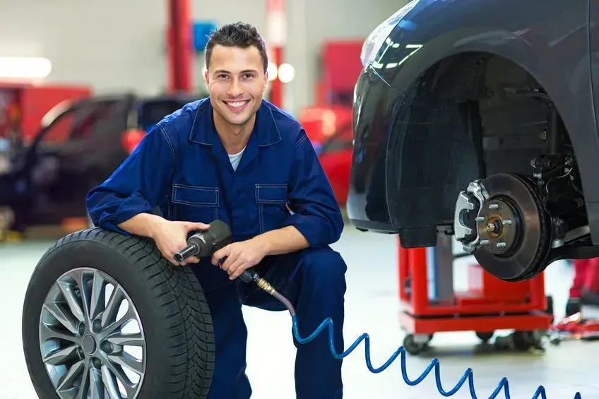 A Mechanic Is Kneeling Next to a Tire in a Garage | DJ's Auto Repair