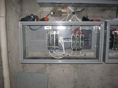 Un quadro elettrico industriale con cavi e componenti a vista, installato su una parete di cemento grigio.