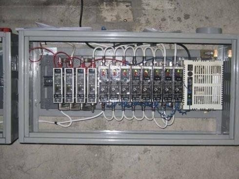 Un quadro elettrico aperto contenente una fila di interruttori automatici modulari, cablaggi e una grande unità di controllo bianca.