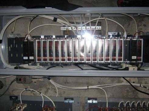 Una fila di unità di controllo modulari elettroniche con cavi bianchi, racchiuse in un contenitore metallico e montate sopra pannelli di cablaggio a parete.