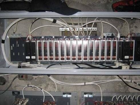 Una fila di unità di controllo industriali modulari montate in un rack elettrico grigio, con vari cavi collegati sopra e sotto.