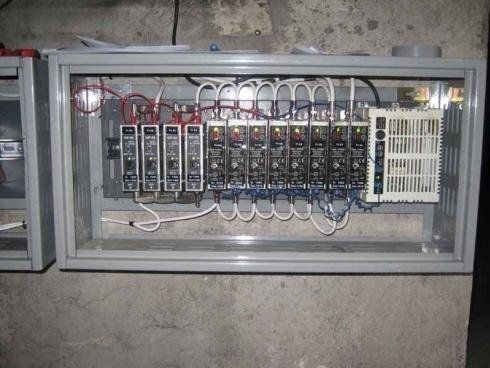Quadro elettrico di controllo con relè modulari multipli e alimentatore, montato all'interno di un contenitore metallico grigio.