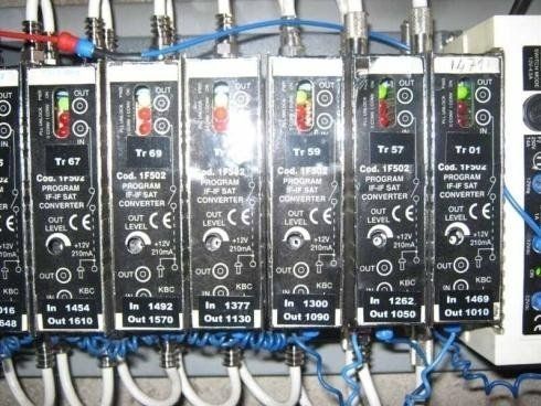 Una fila di convertitori di segnale elettronici per la TV satellitare, montati uno accanto all'altro con cavi coassiali e fili blu collegati.