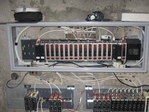 Un quadro di controllo industriale montato su una parete di cemento, composto da diverse unità modulari con cablaggio e involucri grigi.