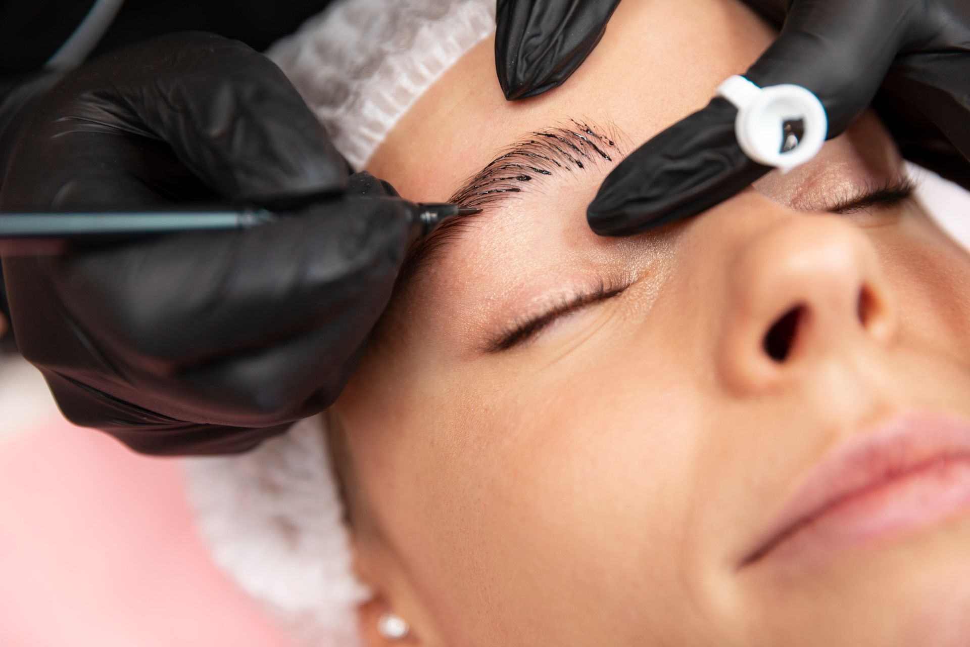 Person receiving eyebrow microblading; black gloves, close-up.