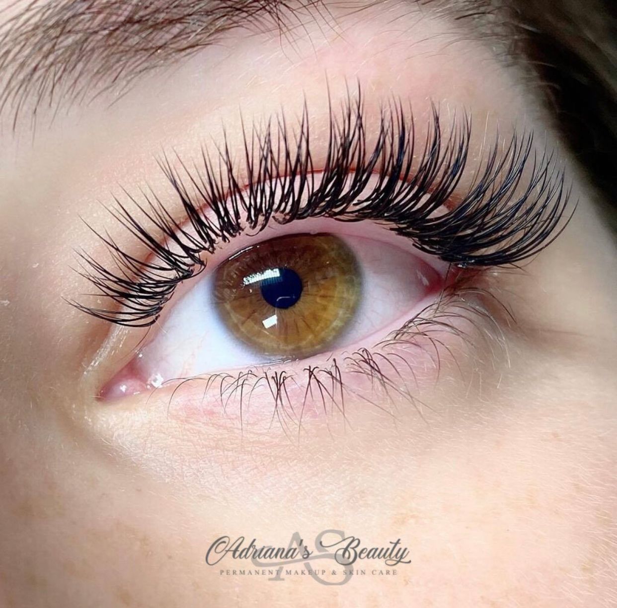 Close-up of a brown eye with long, dark eyelash extensions. The eye is open, and skin is fair.