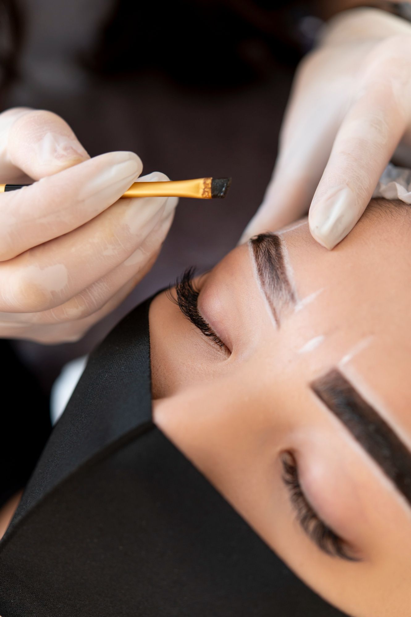 Person getting eyebrow makeup applied with a brush by gloved hands.