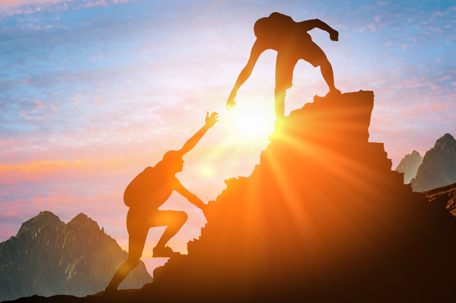 A person helping a friend reach the peak of a mountain.