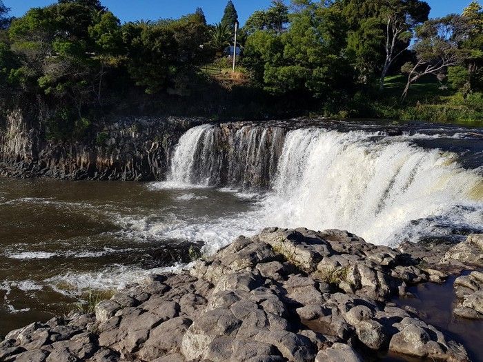 A waterfall is surrounded by rocks and trees on a sunny day
