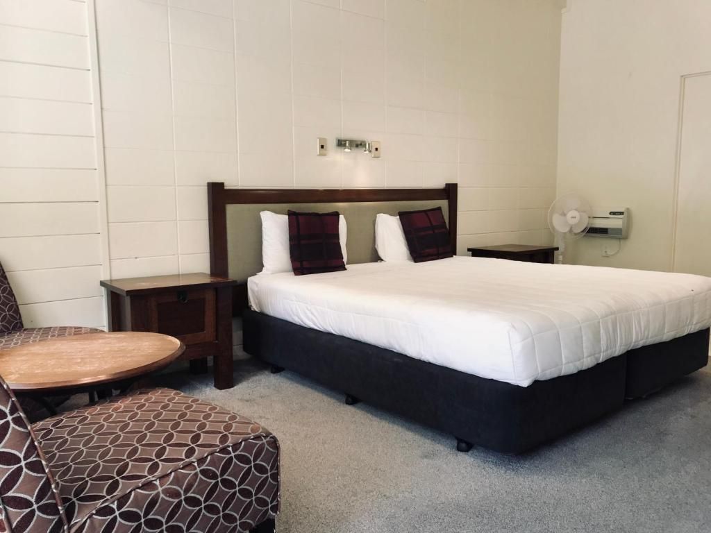 A hotel room with a bed , chair , table and nightstand.