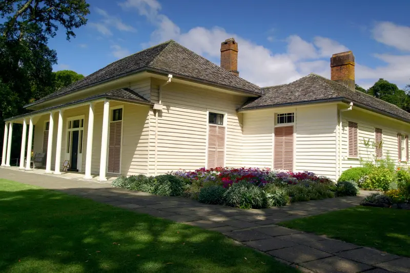 A large white house with a porch and flowers in front of it.