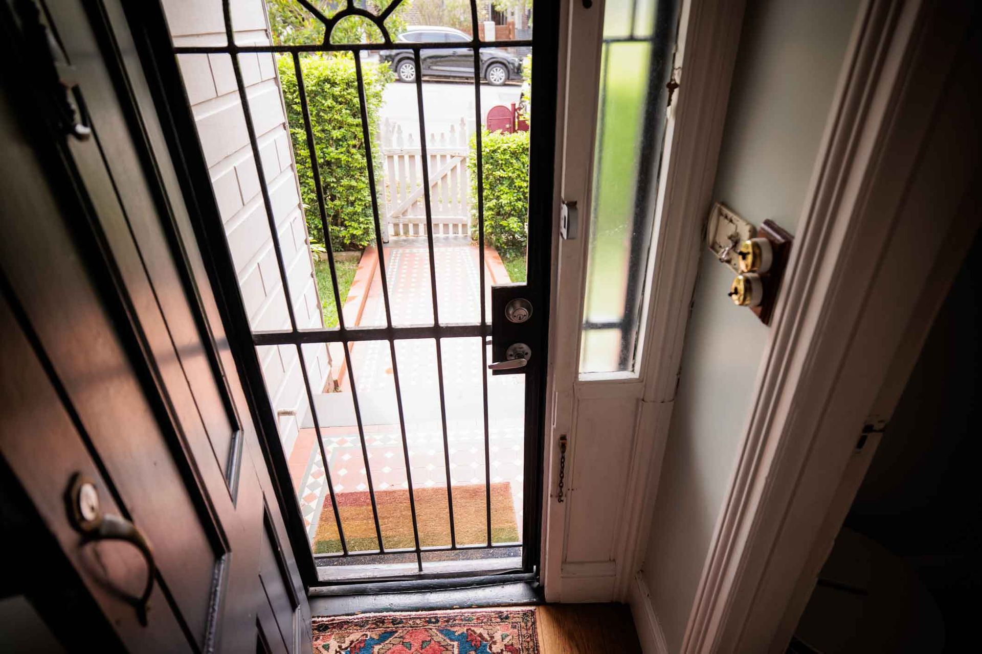 A door with a wrought iron gate is open to a brick walkway.