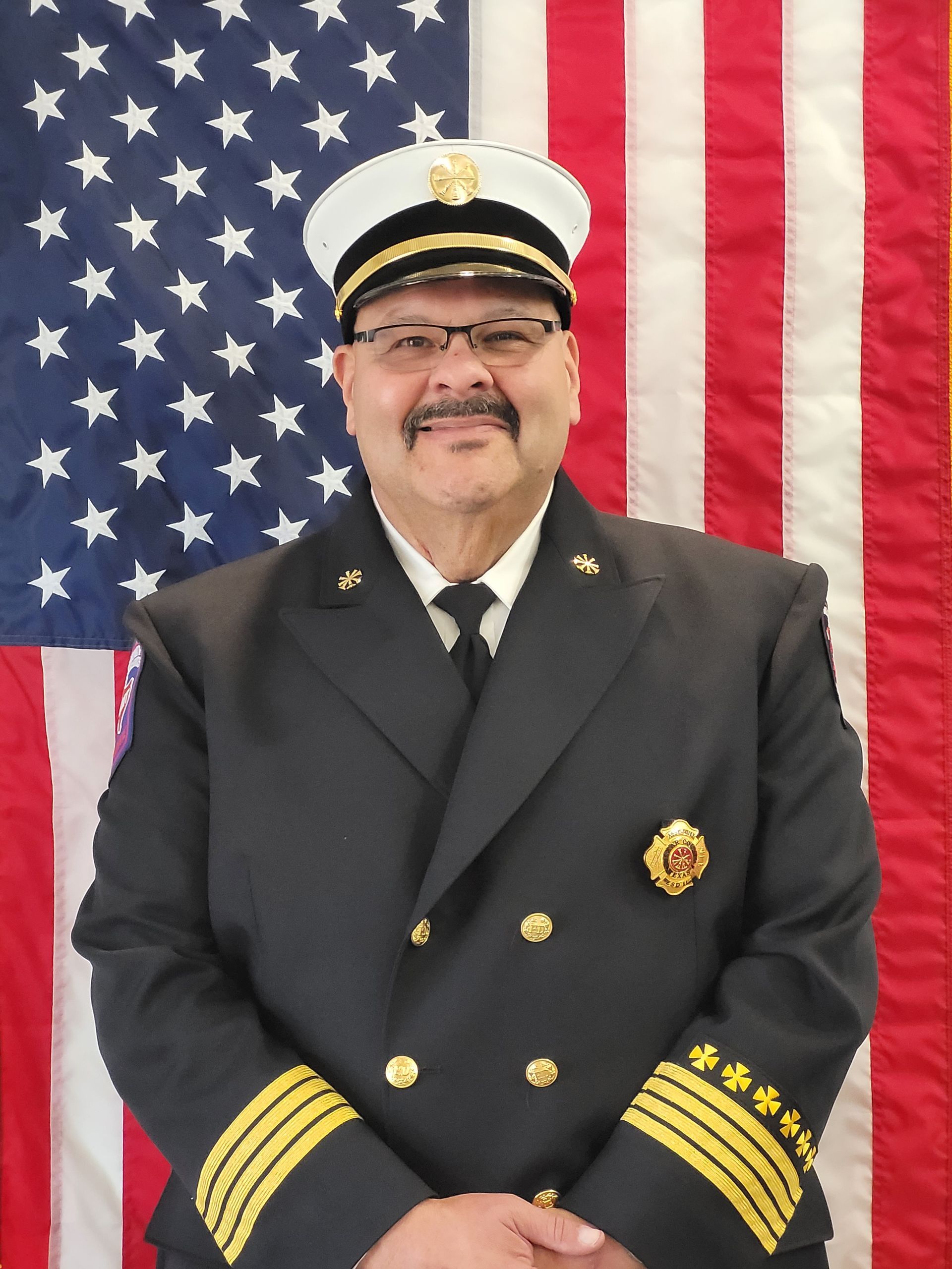 A man in a military uniform stands in front of an American flag