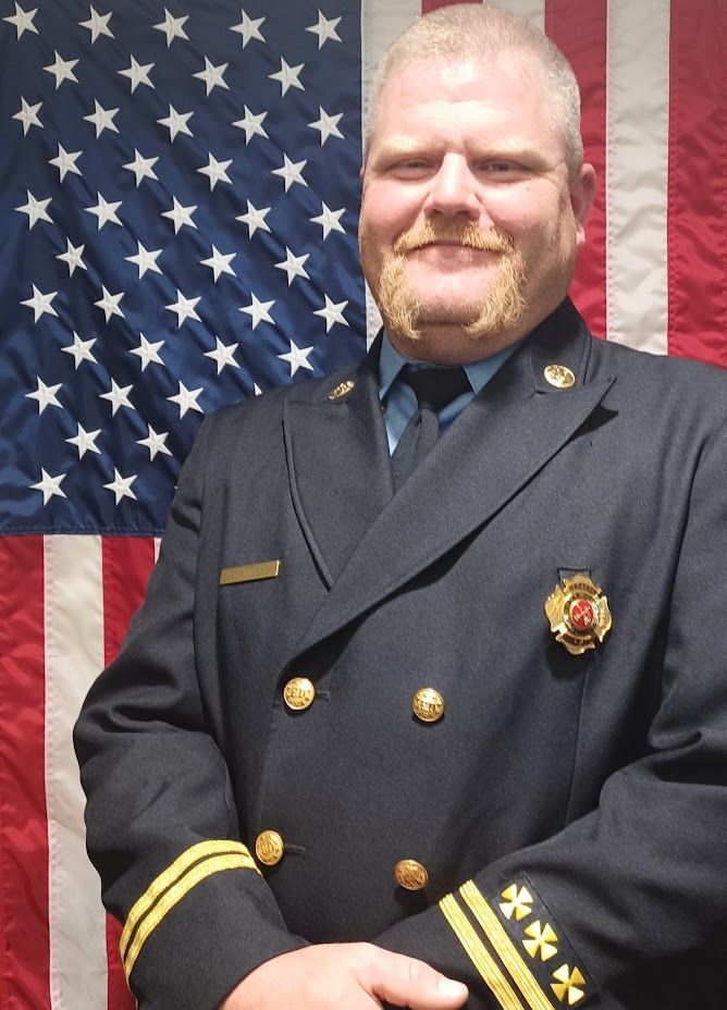 A man in a uniform stands in front of an American flag