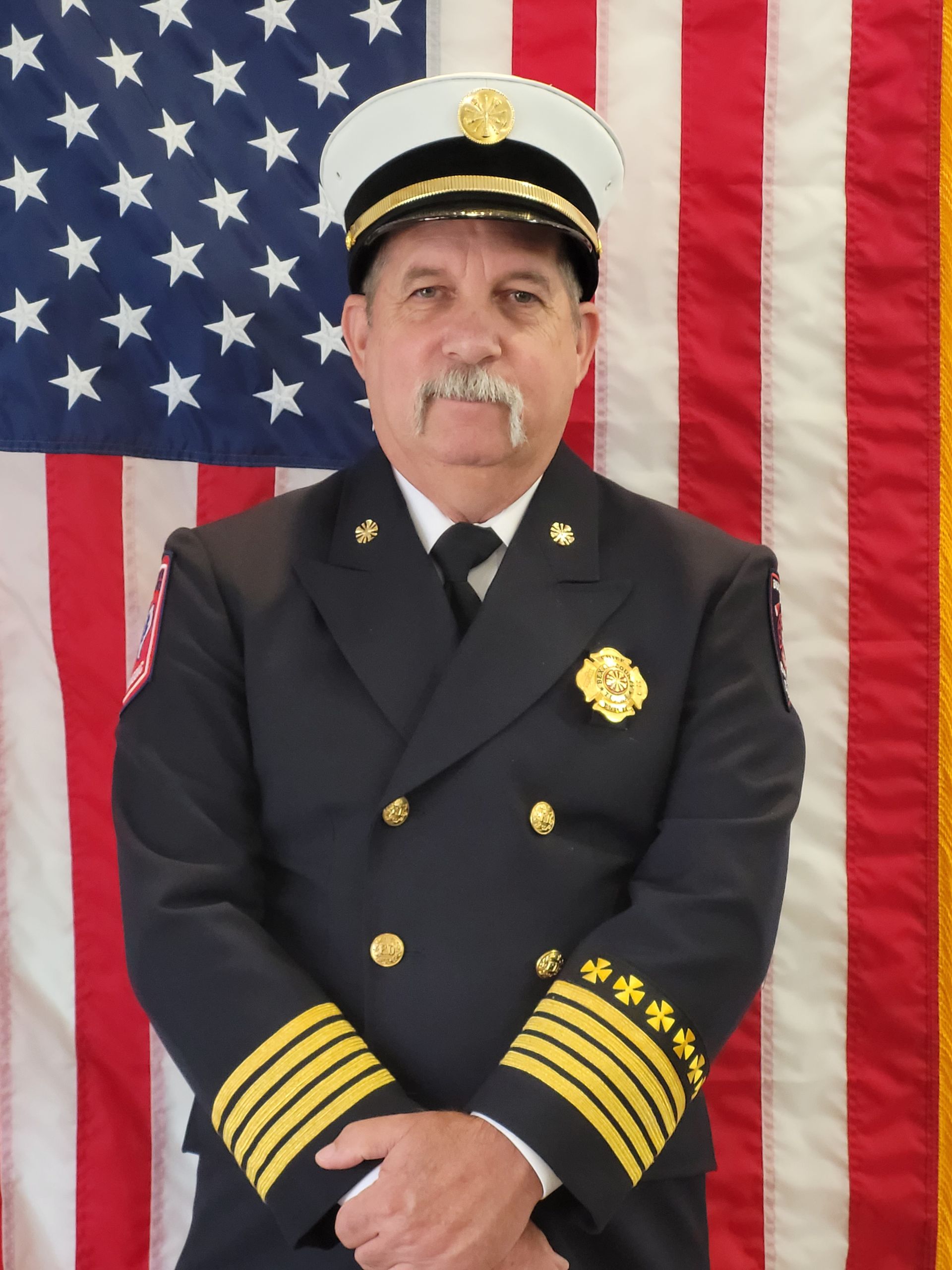 A man in a uniform stands in front of an American flag