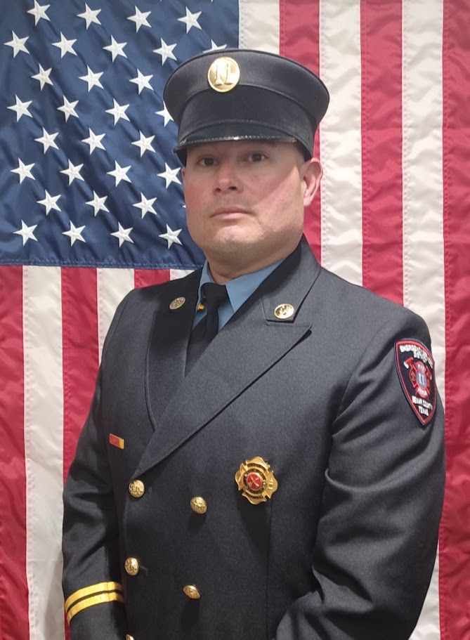 A man in a uniform stands in front of an American flag