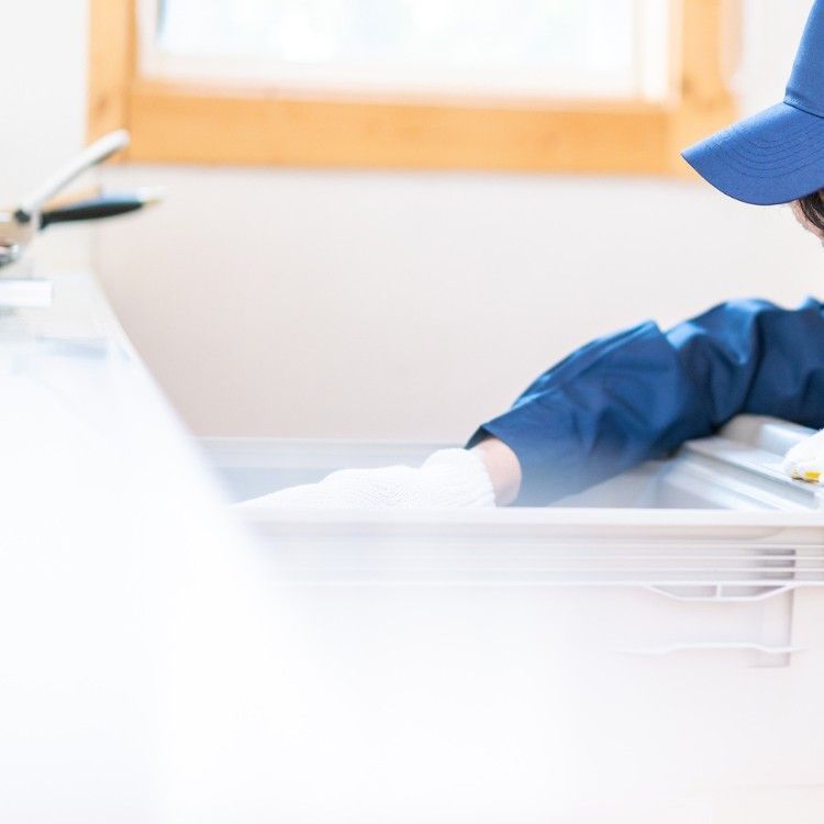 A person in a blue uniform and cap wears white gloves while cleaning or inspecting a white kitchen drawer.