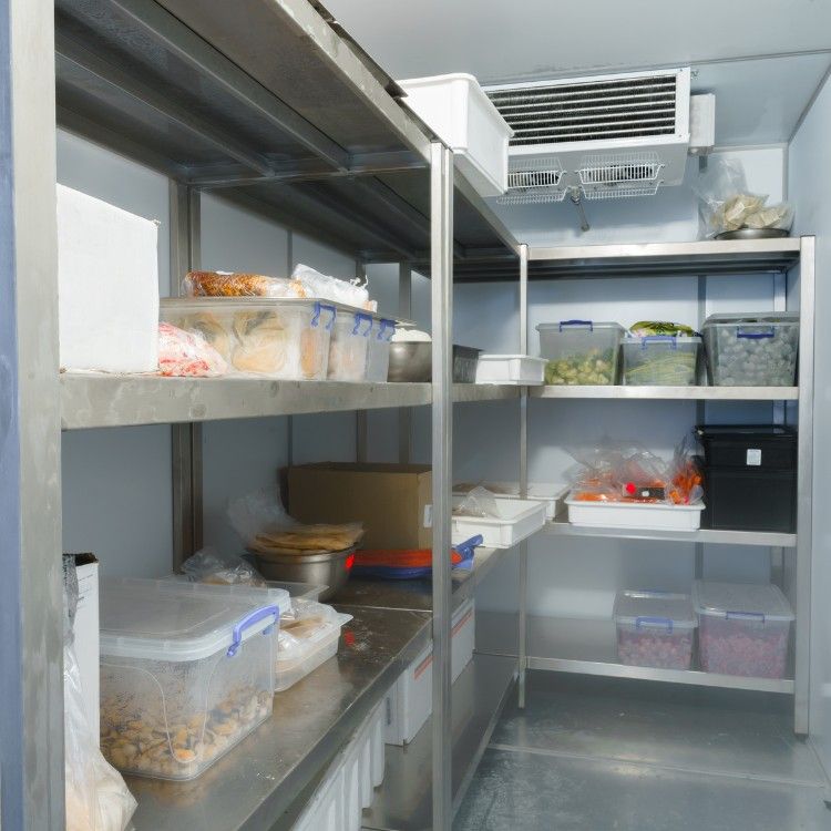 Stainless steel shelving inside a walk-in freezer holds various food storage containers, boxes, and a cooling unit.