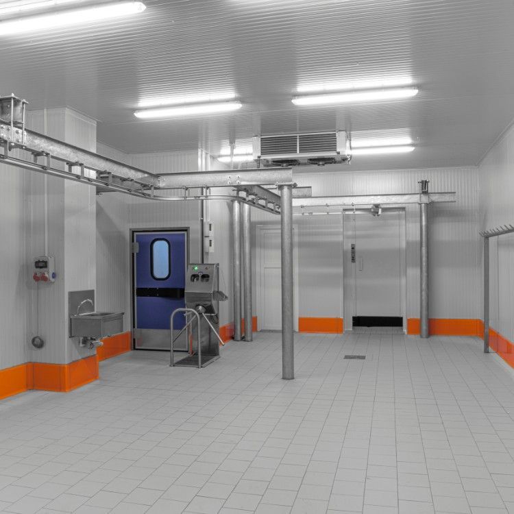 A clean, industrial food processing room with white tiled walls, orange baseboards, an overhead rail system, and a sink.