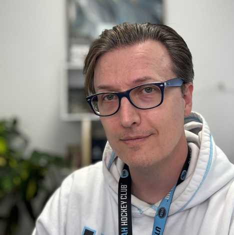 Man wearing glasses and a hoodie, looking at the camera. He has a lanyard that says 