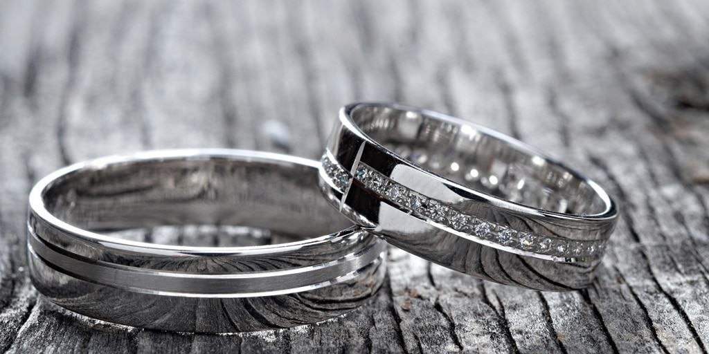Two silver wedding rings on a weathered wooden surface. One has a black and diamond accent.