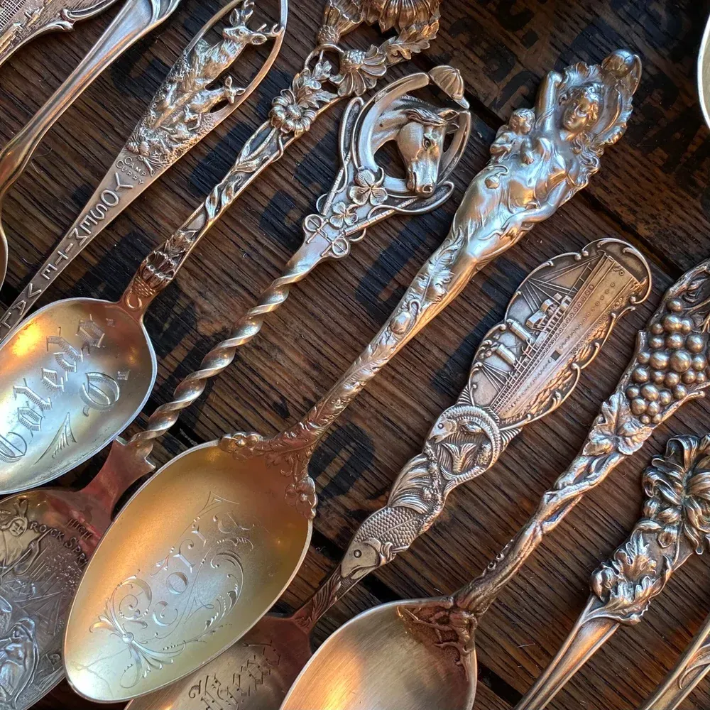 Close-up of antique silver spoons with ornate handles, arranged on a wooden surface.
