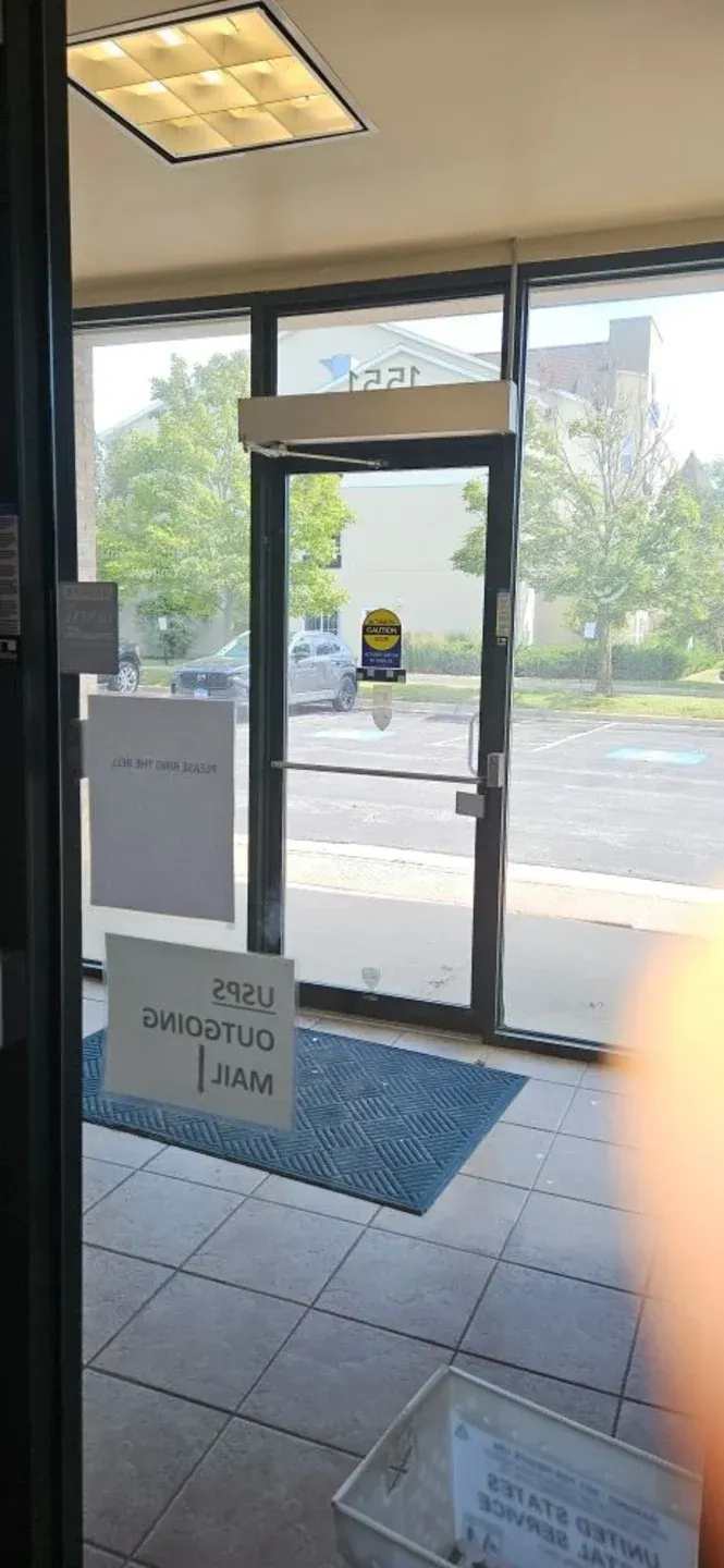 Store entrance with glass door, welcome sign, and street view outside under bright daylight.