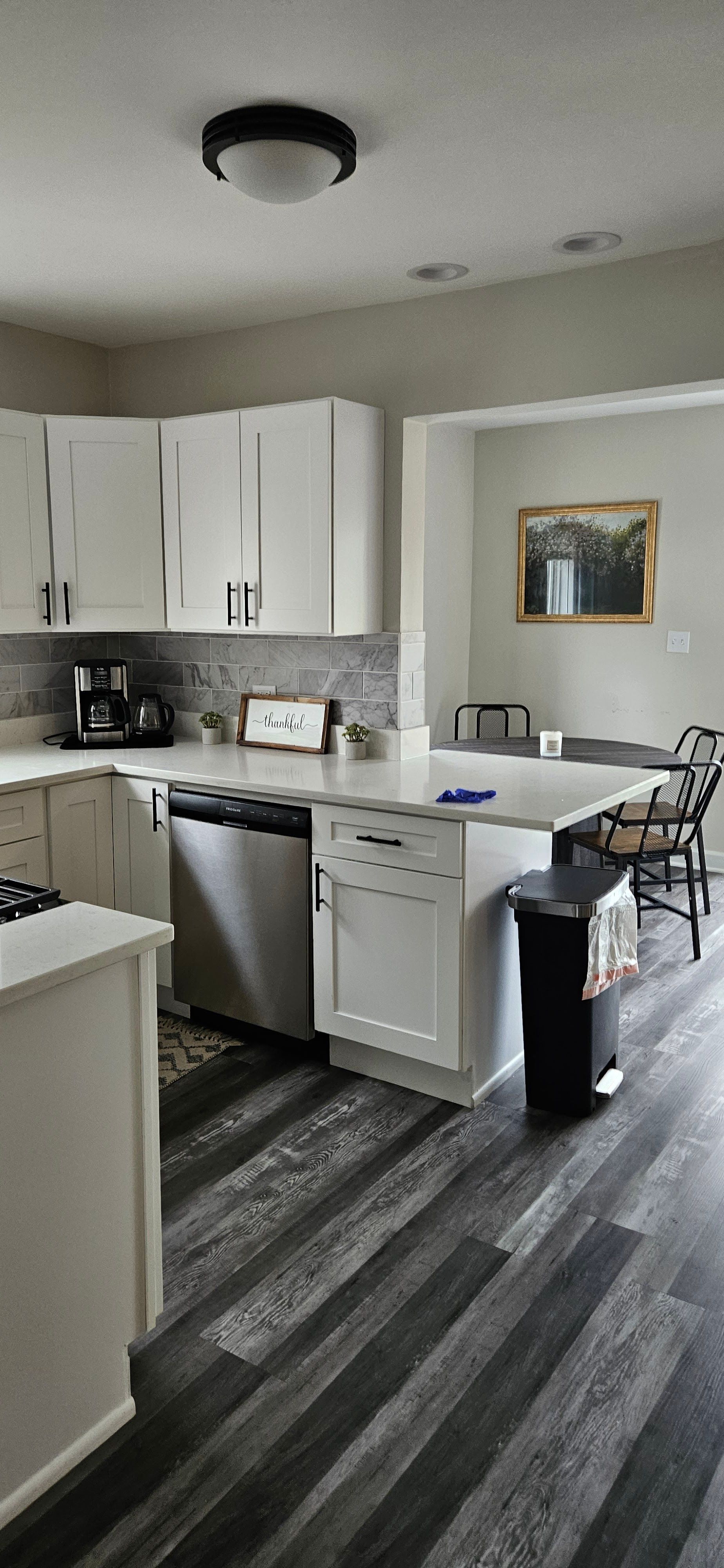 Modern kitchen with white cabinets, gray flooring, black fridge, and a small dining table by the window