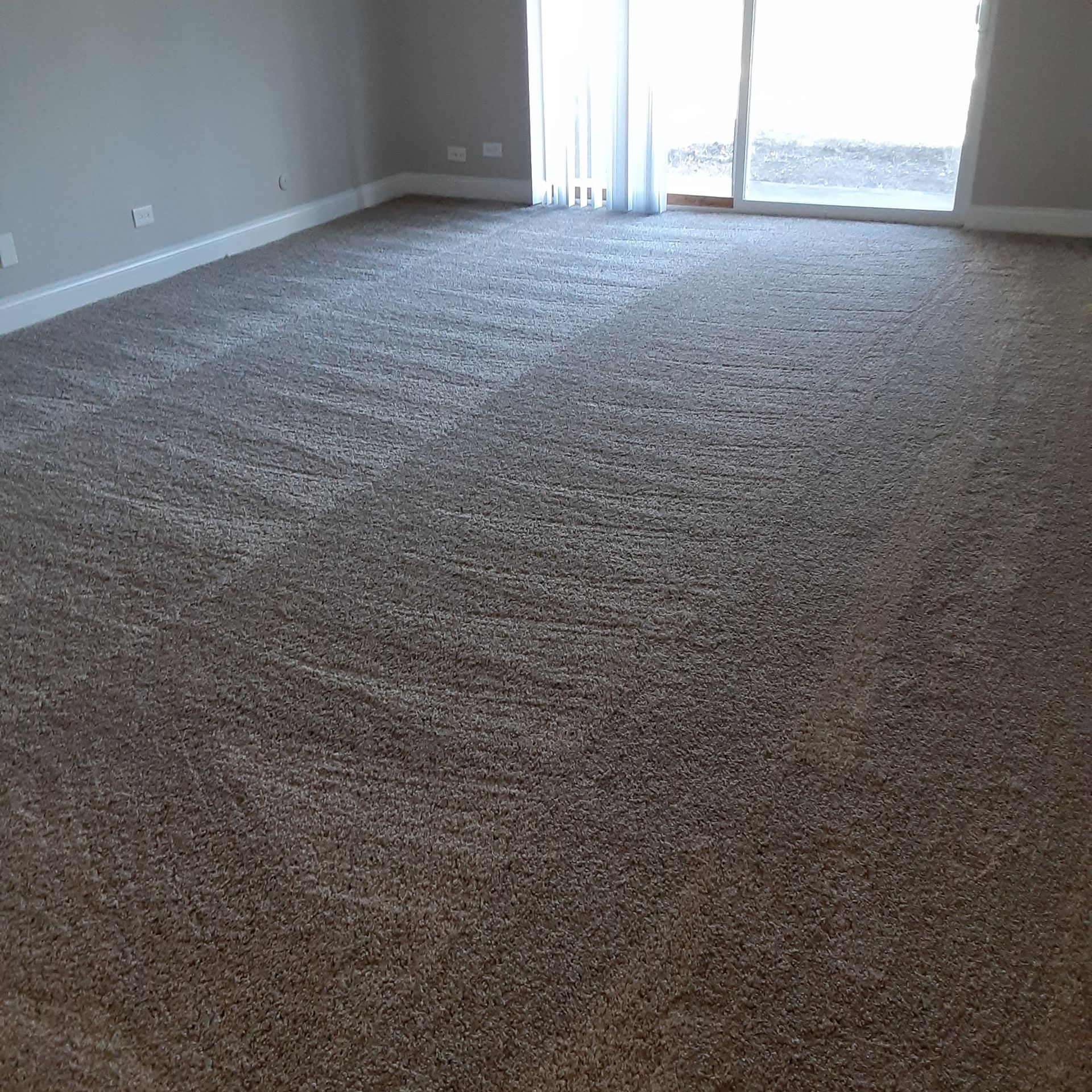 Empty carpeted living room with beige walls and sliding glass doors letting in daylight