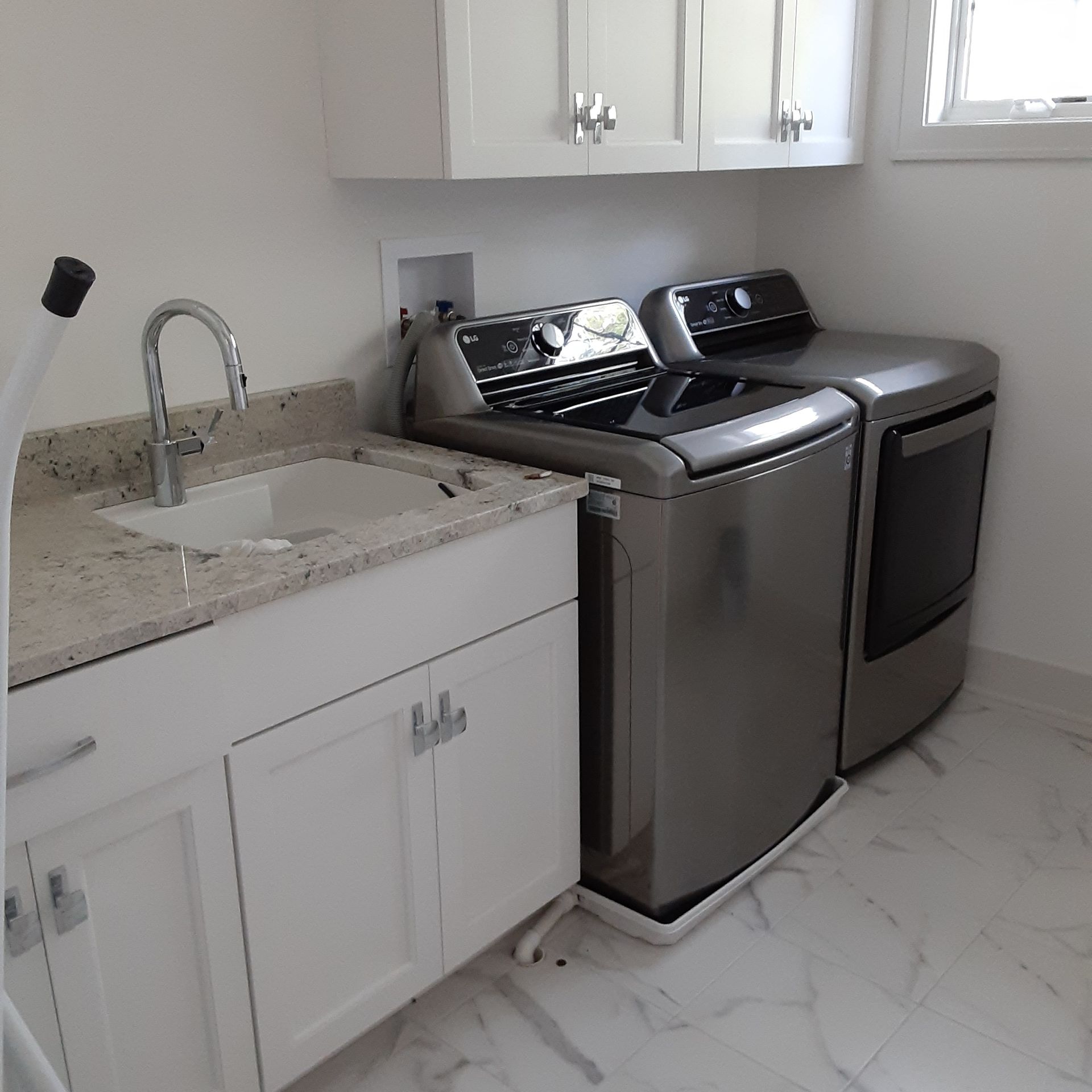 Bright laundry room with white sink cabinets and stainless steel washer and dryer on a tiled floor