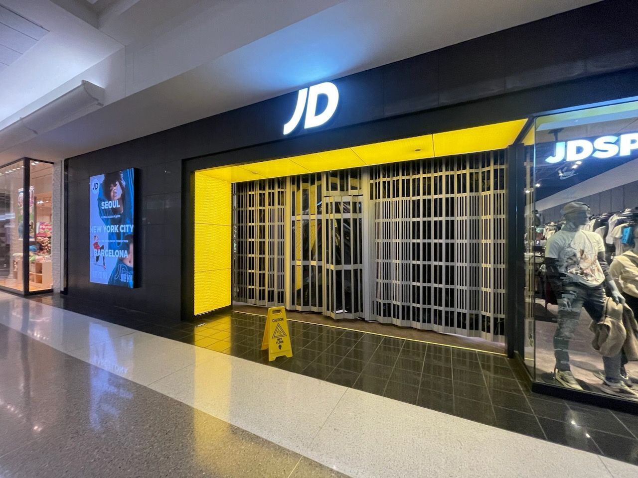 Closed JD sports store with yellow shutter in a shopping mall corridor
