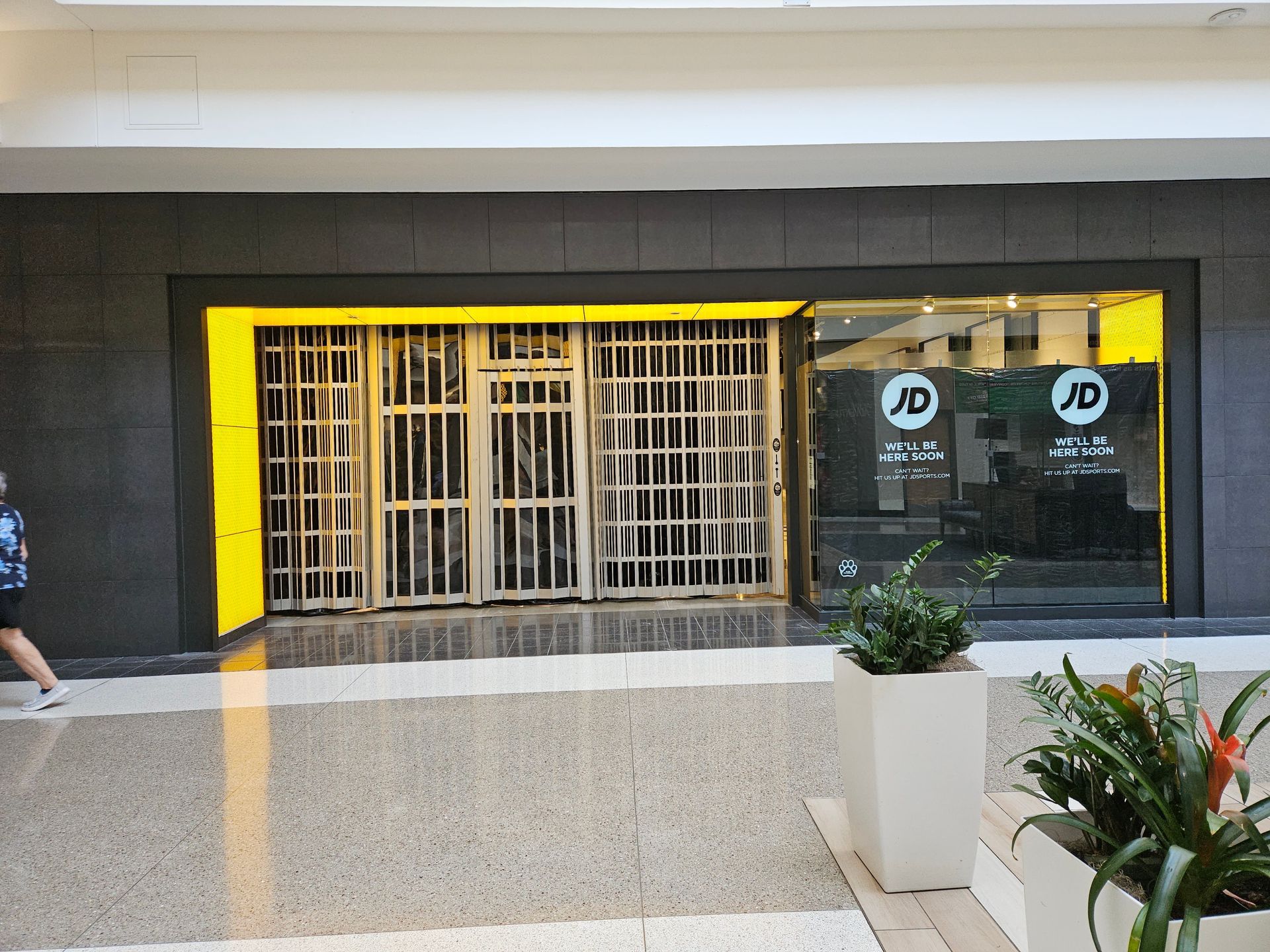Closed storefront with yellow trim and barred entrance in a shopping mall corridor