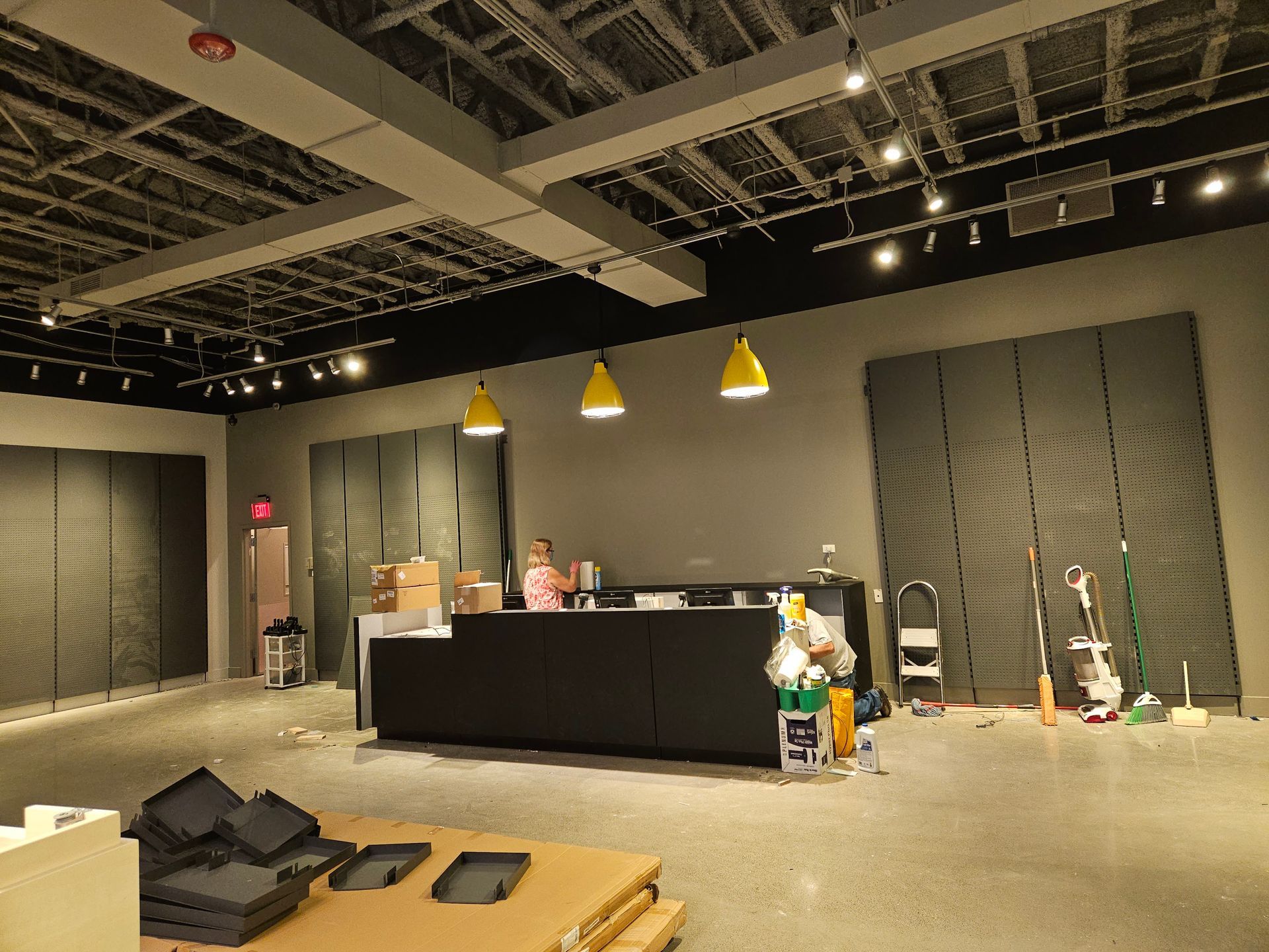 Empty retail space with a black counter, hanging yellow lights, and cleaning supplies on the floor