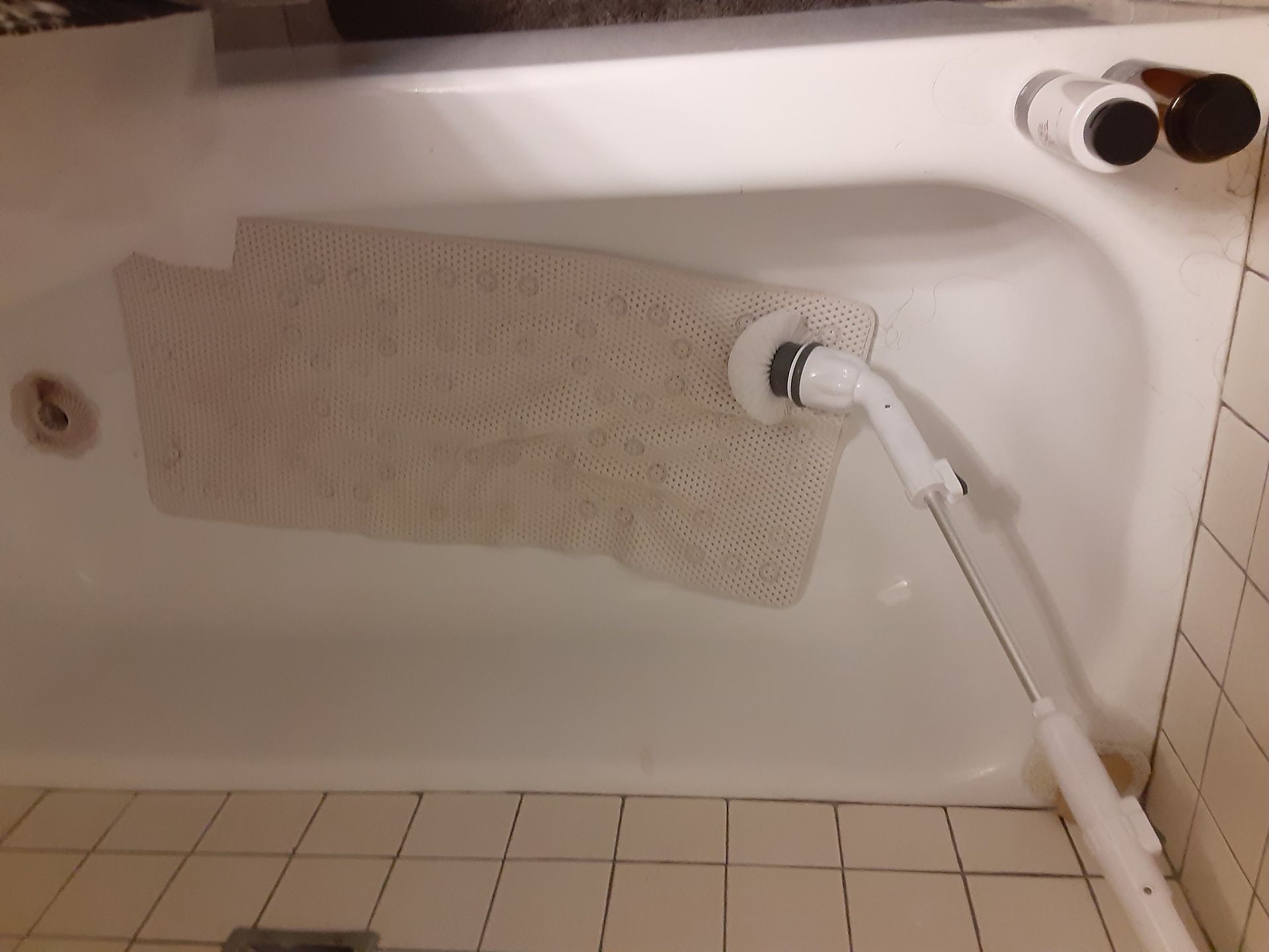 Bathtub with a bath mat and shower hose in a tiled bathroom, shown sideways.