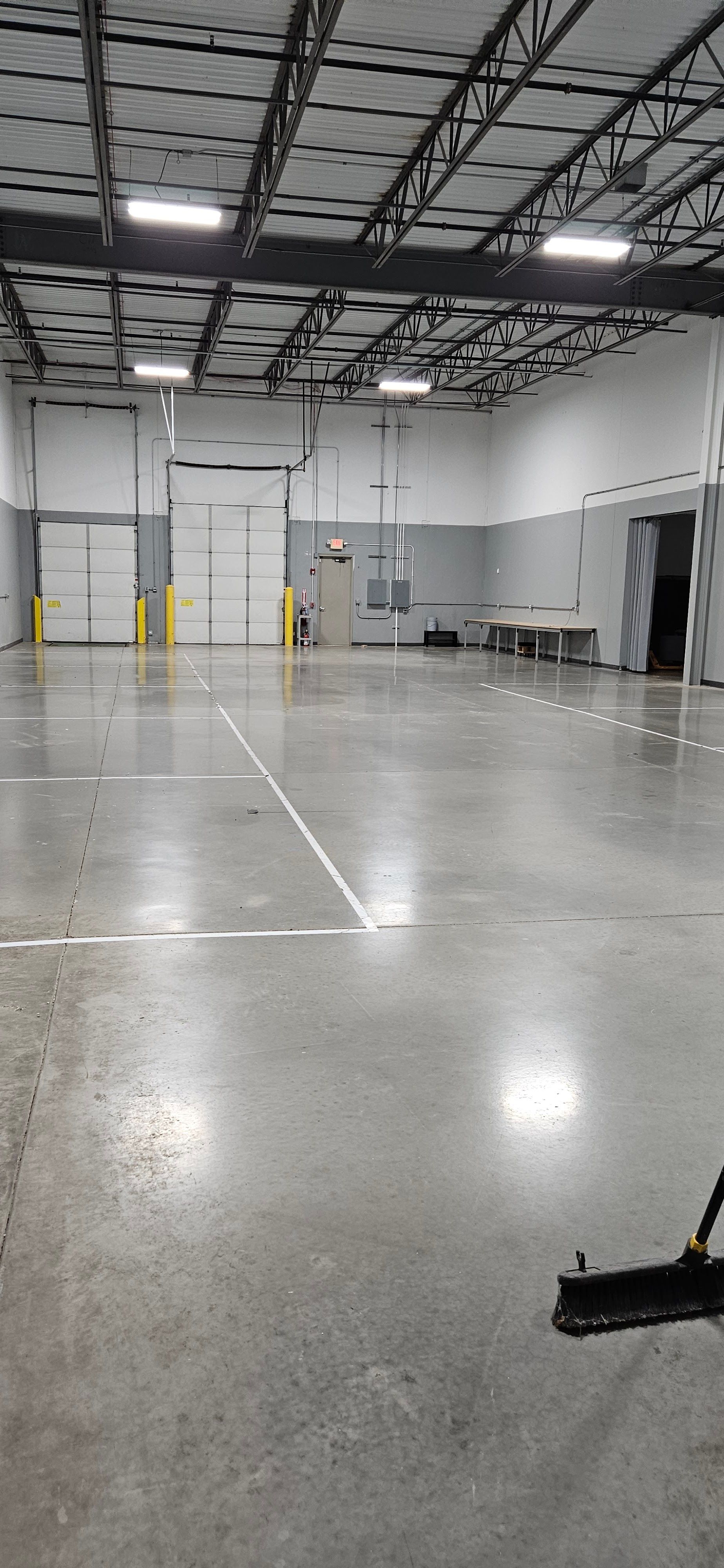 Empty industrial warehouse with polished concrete floor, metal ceiling beams, and large overhead doors