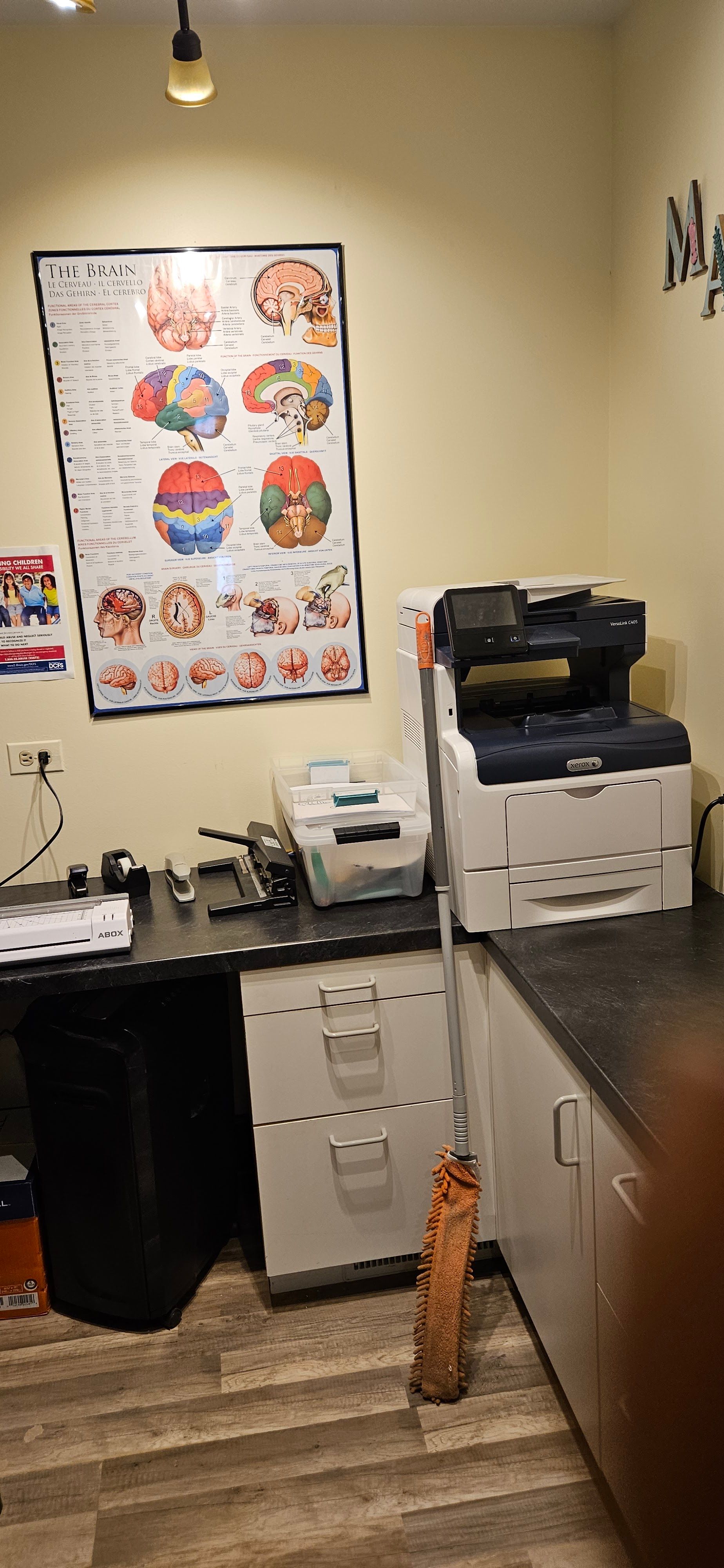 Small office or clinic with cabinets, equipment, posters, and a countertop in the foreground.