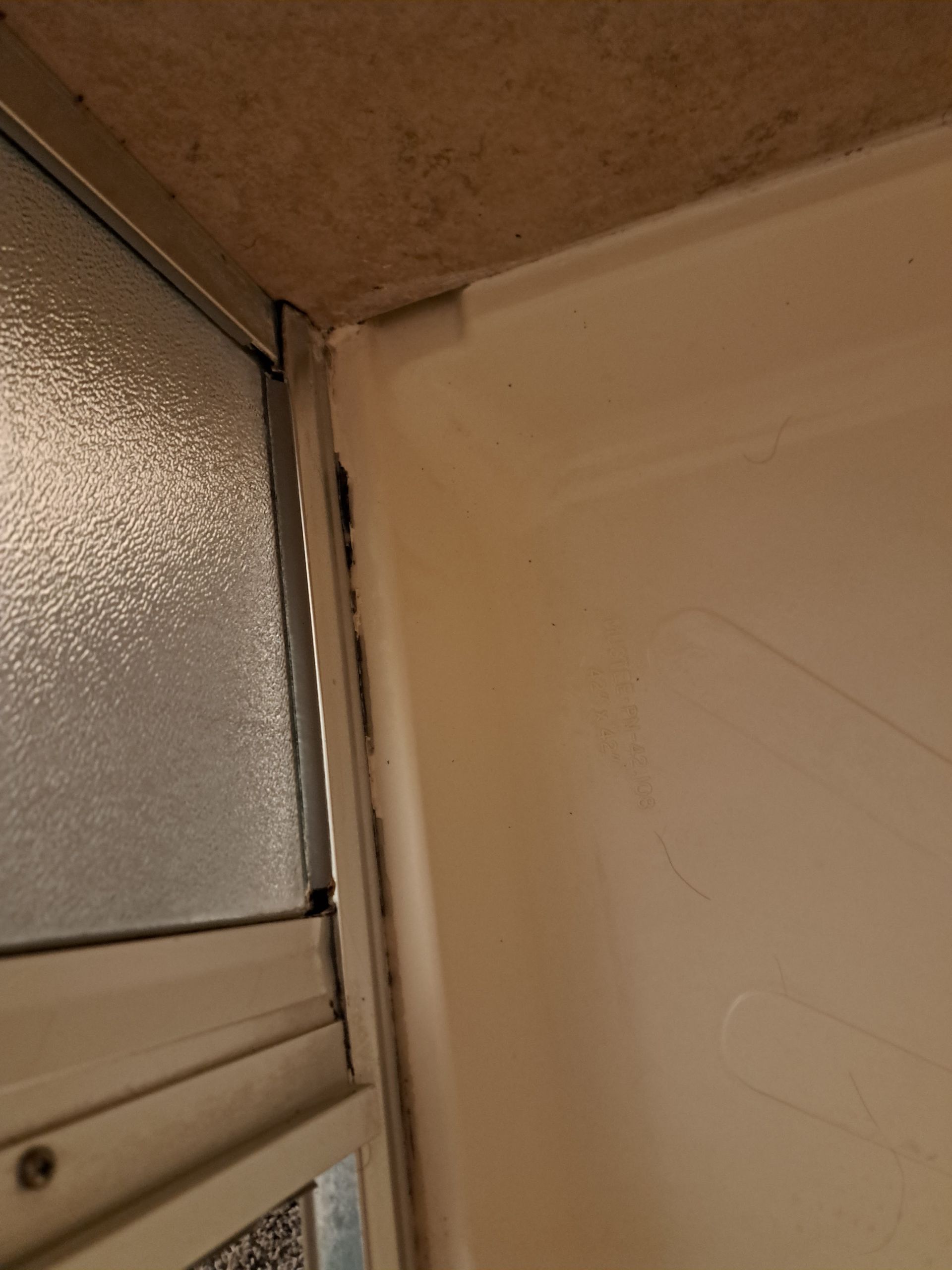 Close-up of a bathroom shower corner with peeling caulk and a frosted glass door