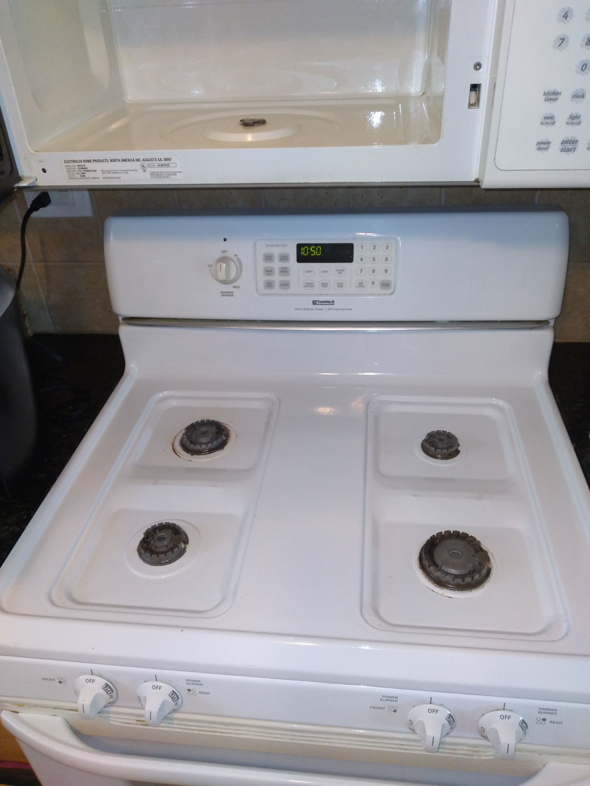 White electric stove with four coil burners and a control panel beneath a microwave cabinet.
