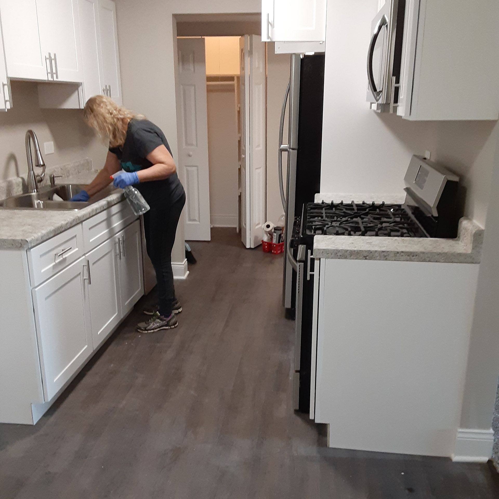 Person washing dishes in a modern kitchen with white cabinets and gray flooring.