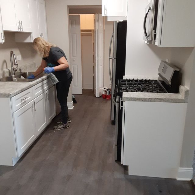 Person cleaning a white kitchen sink in a narrow kitchen with dark wood floors.