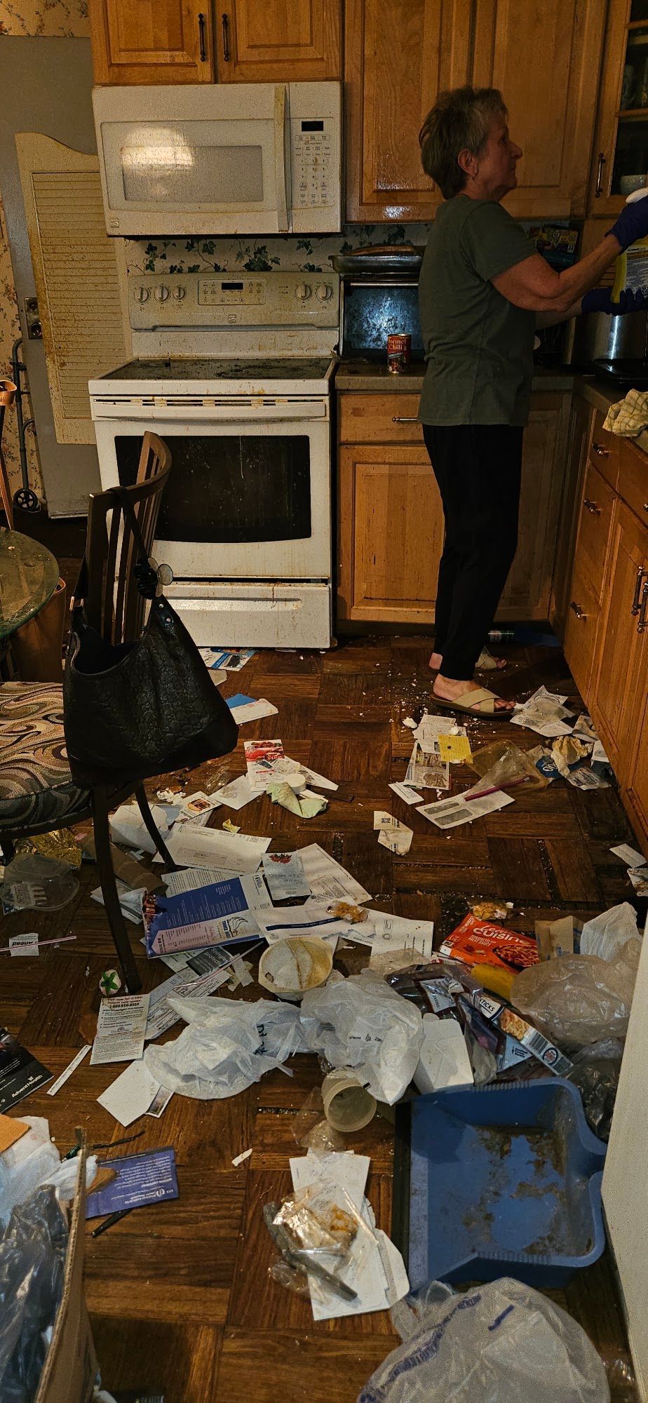 Messy kitchen with papers and debris on the floor, person standing near the stove and cabinets