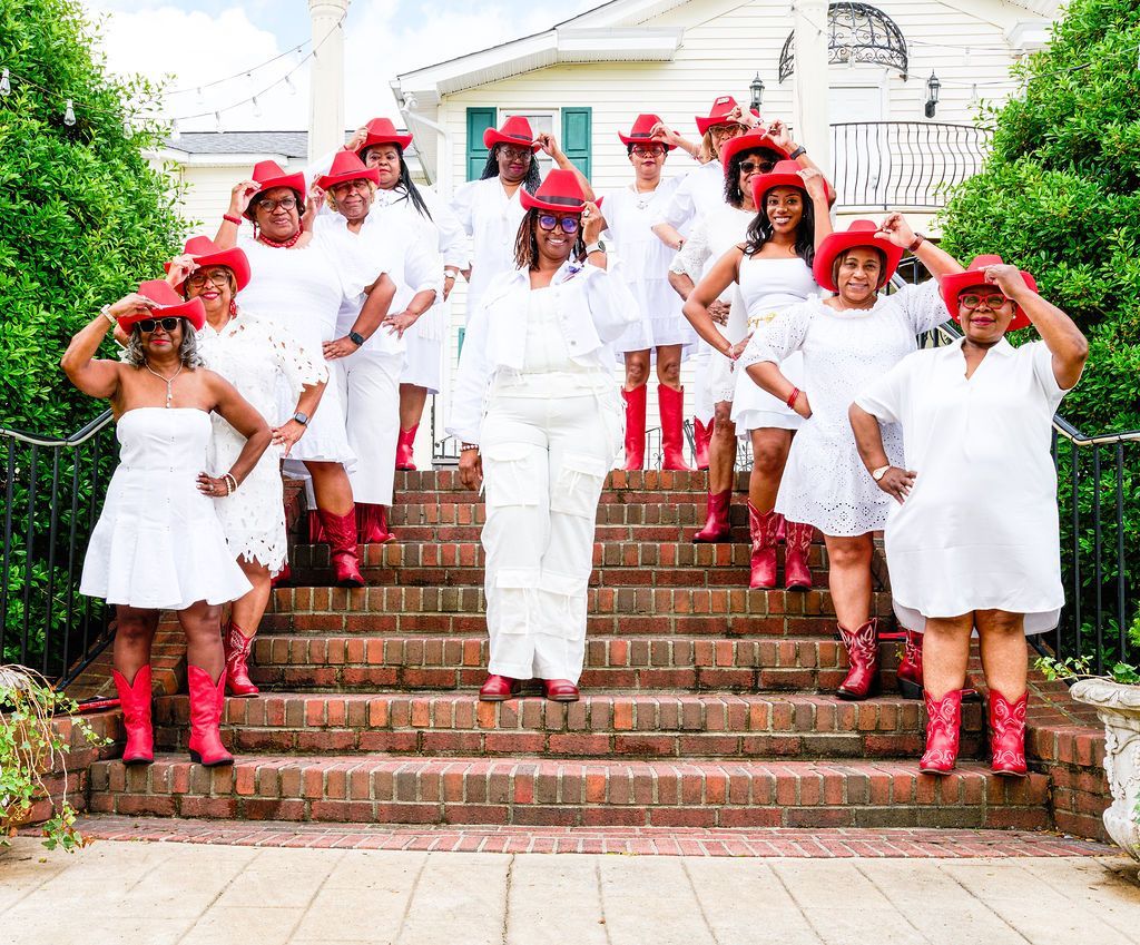 Group of people in white outfits and red hats and boots posing on brick steps.