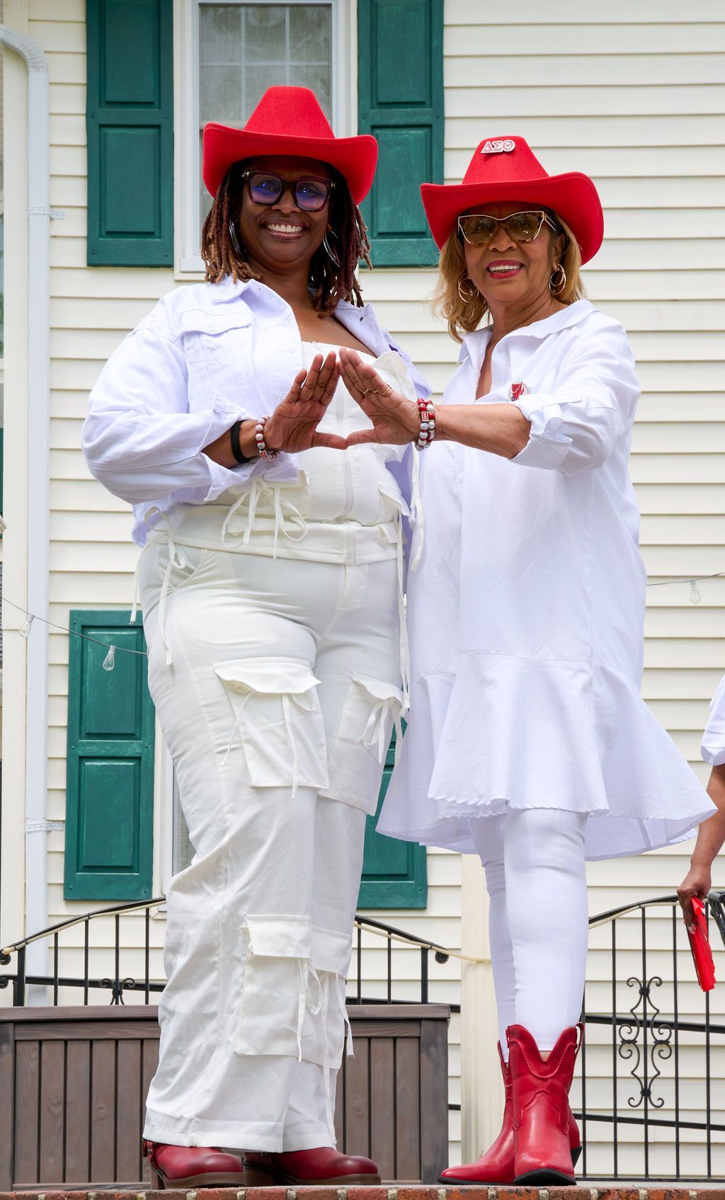 Two women in red cowboy hats and white outfits, forming a triangle with their hands.
